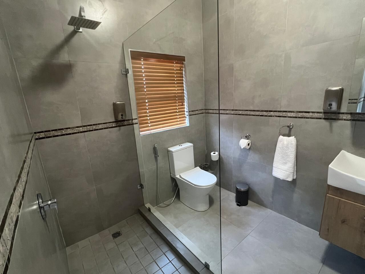 Un baño moderno con cabina de ducha de vidrio, inodoro, lavamanos y toallero.