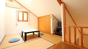 Una habitación con suelo de tatami, una mesa baja, una puerta de madera y una escalera.