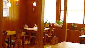 Un interior de madera con mesas y sillas, plantas en macetas y lámparas colgantes.