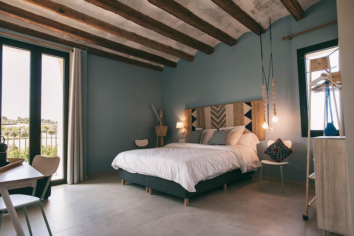 A bedroom with a bed, a chair, a table, and a view of the outdoors.