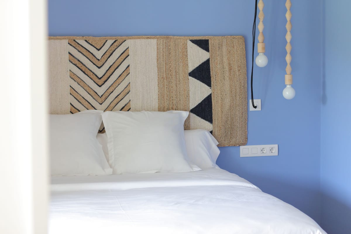 A bed with white bedding, a headboard with a geometric patterned headboard, and a wall socket.