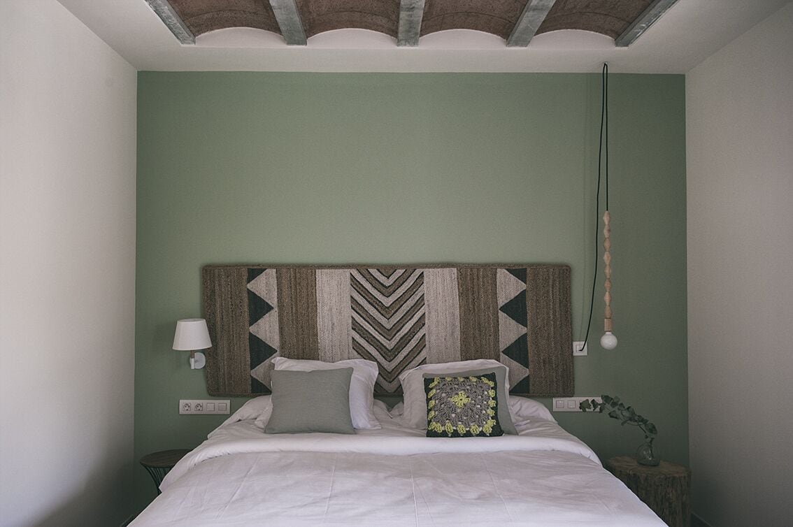 A bedroom with a bed, a wall-mounted lamp, and a hanging light fixture.