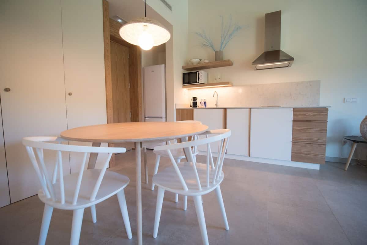 A modern kitchen with a round wooden table and white chairs, a microwave, and a built-in oven.