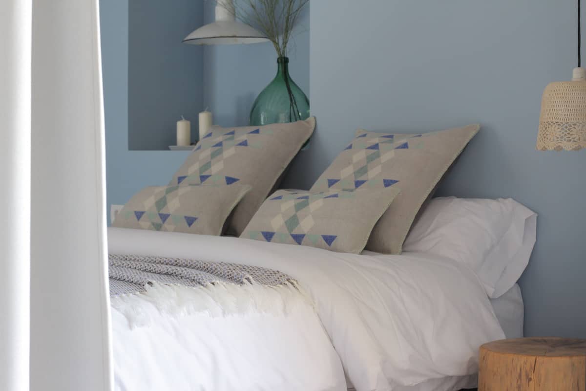 A neatly made bed with patterned pillows, a bedside lamp, and a vase on a nightstand.