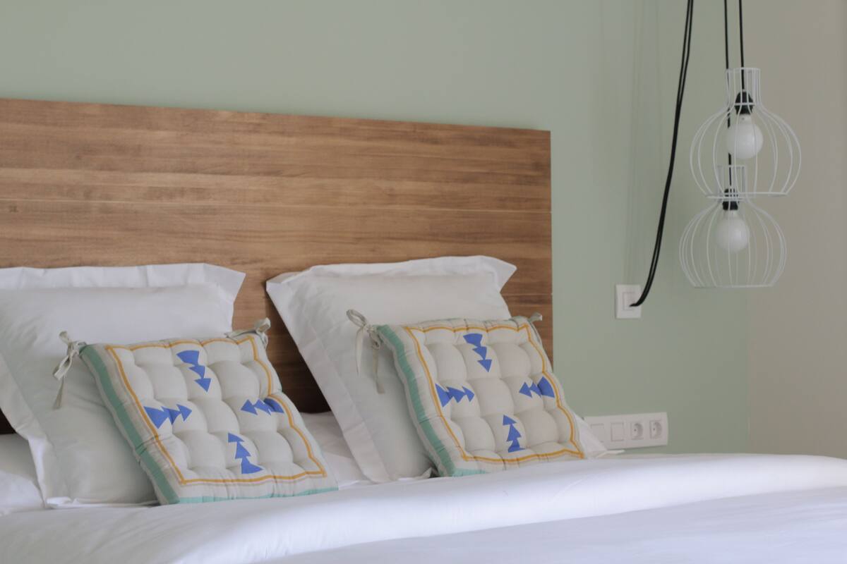 A neatly made bed with white bedding, two decorative pillows with blue and yellow patterns, and a wooden headboard.