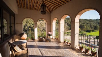 A covered patio with wicker furniture, stone pillars, and potted plants.