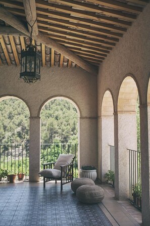 A covered outdoor seating area with a wooden ceiling, stone columns, and a view of a forested landscape. - Can Alemany (Santa Margarida de Montbui)
