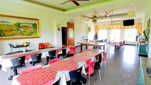 A dining area with tables set for multiple people, a painting on the wall, and a television mounted on the wall. - Rice Countryside B&B (Dongshan)