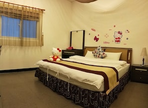 Una cama bien hecha con un peluche de Hello Kitty, una almohada estampada y una mesita de noche con una lámpara.