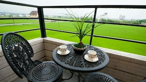 A balcony with two ornate chairs and a small table, a potted plant, and a view of a green field. - Rice Countryside B&B (Dongshan)