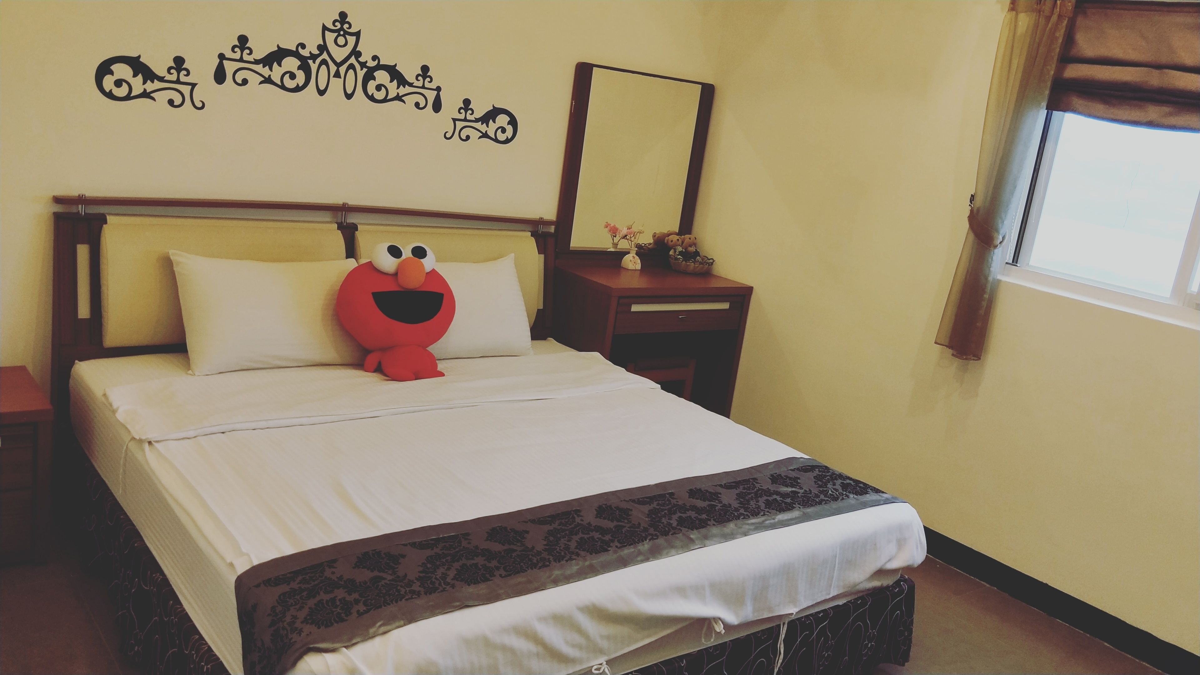 A hotel room with a bed, a nightstand, a dresser, and a window with curtains.
