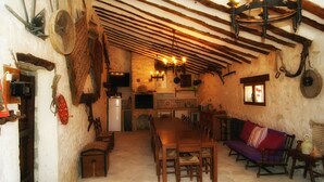 A rustic interior with a wooden dining table, benches, a sofa, and a chandelier.