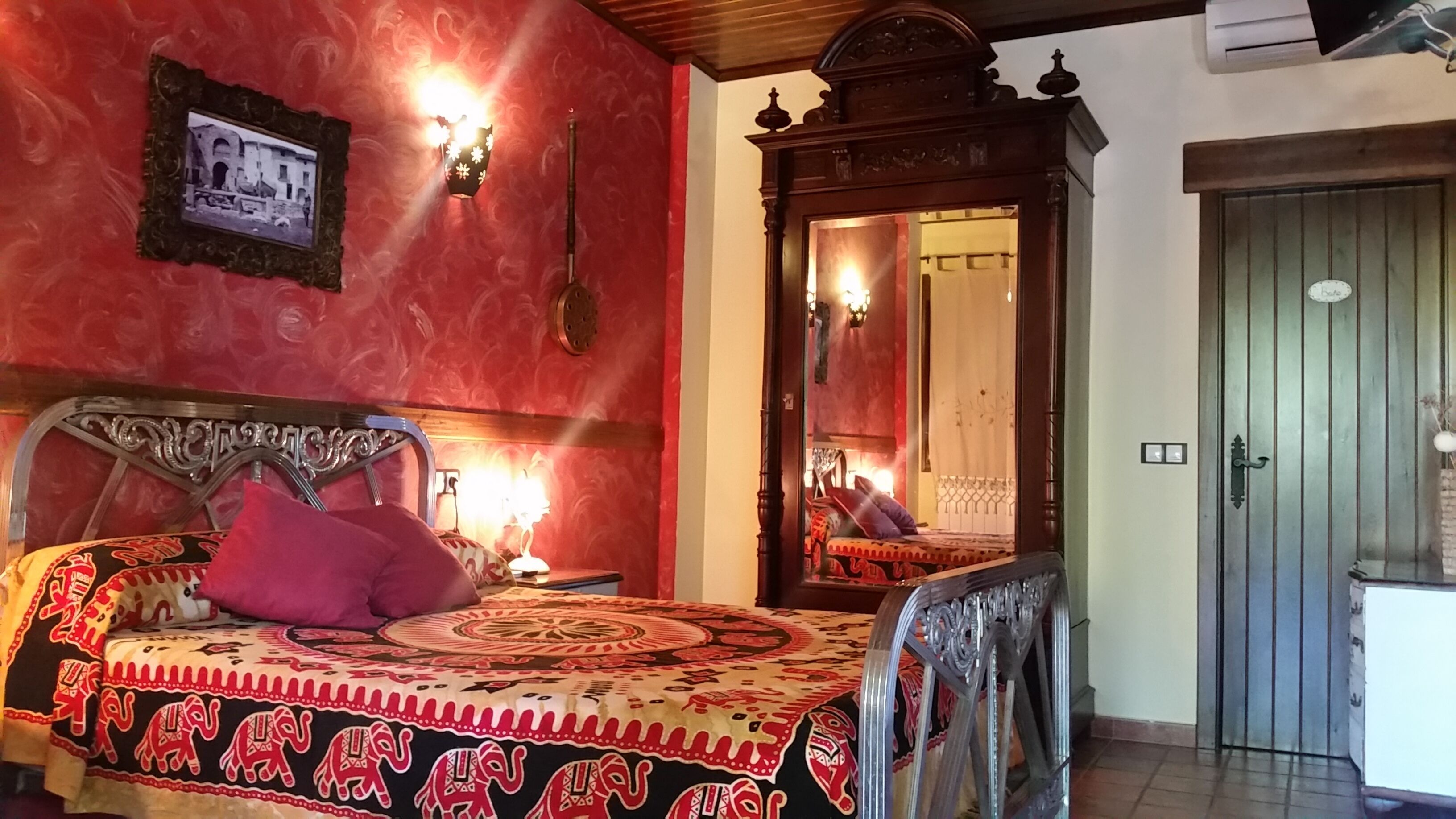 A room with a bed, a nightstand, a mirror, and a door.