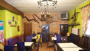 A restaurant with brick walls, a chandelier, and a television. Tables and chairs are arranged for dining.