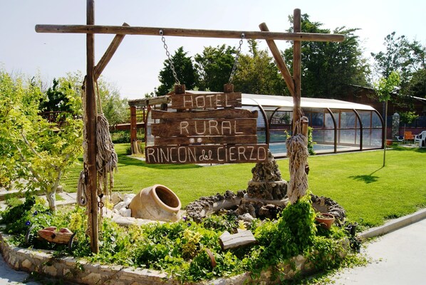 A rustic wooden sign for a rural hotel with a rustic stone well and greenery around.