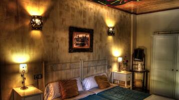 A bedroom with a bed, bedside tables, a nightstand, a framed picture on the wall, and a wardrobe.