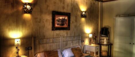 A bedroom with a bed, bedside tables, a nightstand, a framed picture on the wall, and a wardrobe.