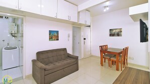 Een knus woongedeelte met kitchenette, een bank, een eettafel met stoelen en een aan de muur bevestigde televisie.