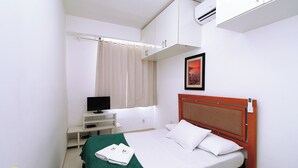 Een hotelkamer met een bed, een bureau met een computer, een televisie en een raam met gordijnen.