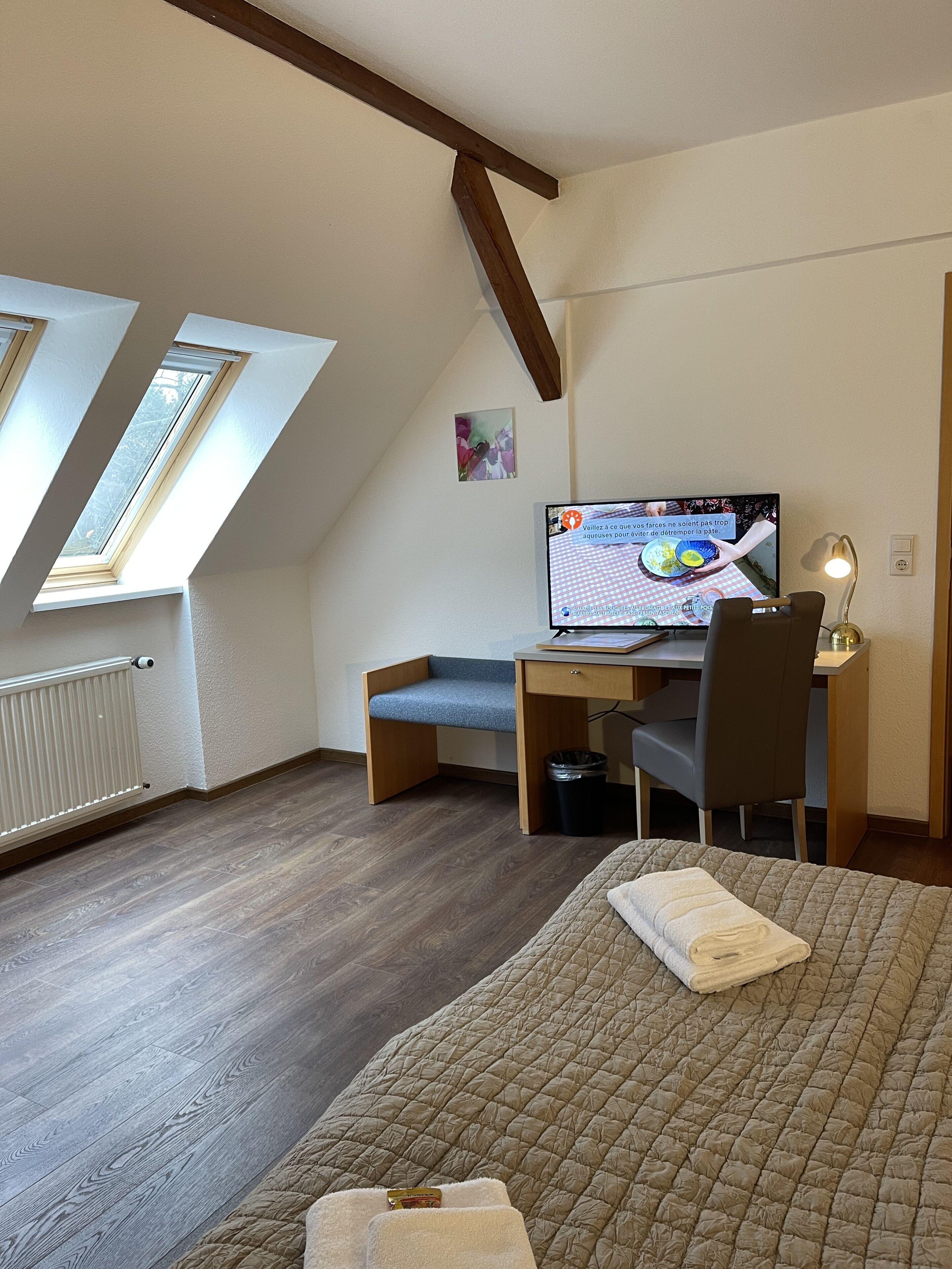 A bedroom with a bed, a desk, a chair, a computer, a window, and a radiator.