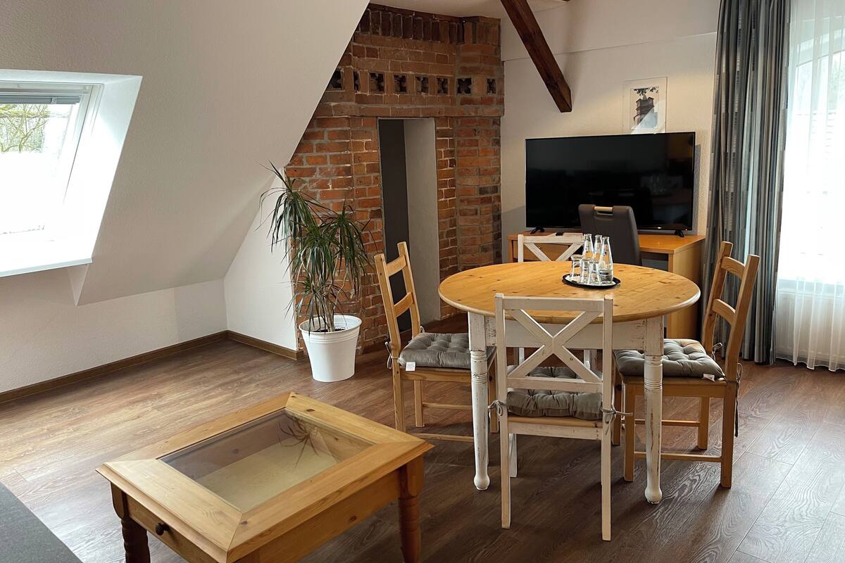 Una sala de estar acogedora con chimenea de ladrillo, una mesa de comedor de madera con sillas, un televisor y una planta en maceta.