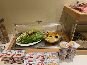 Un bufé con rodajas de pepino, ensalada de frutas y recipientes de yogur.