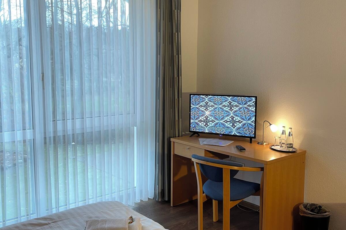 Habitación de hotel con cama, escritorio con computadora, silla y ventana con cortinas.