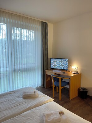 Habitación de hotel con cama, escritorio con computadora, silla y ventana con cortinas.