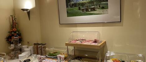 Een buffetopstelling met diverse gerechten en bestek, een lijst met een foto van een bos aan de muur en een decoratieve bloemstelling.