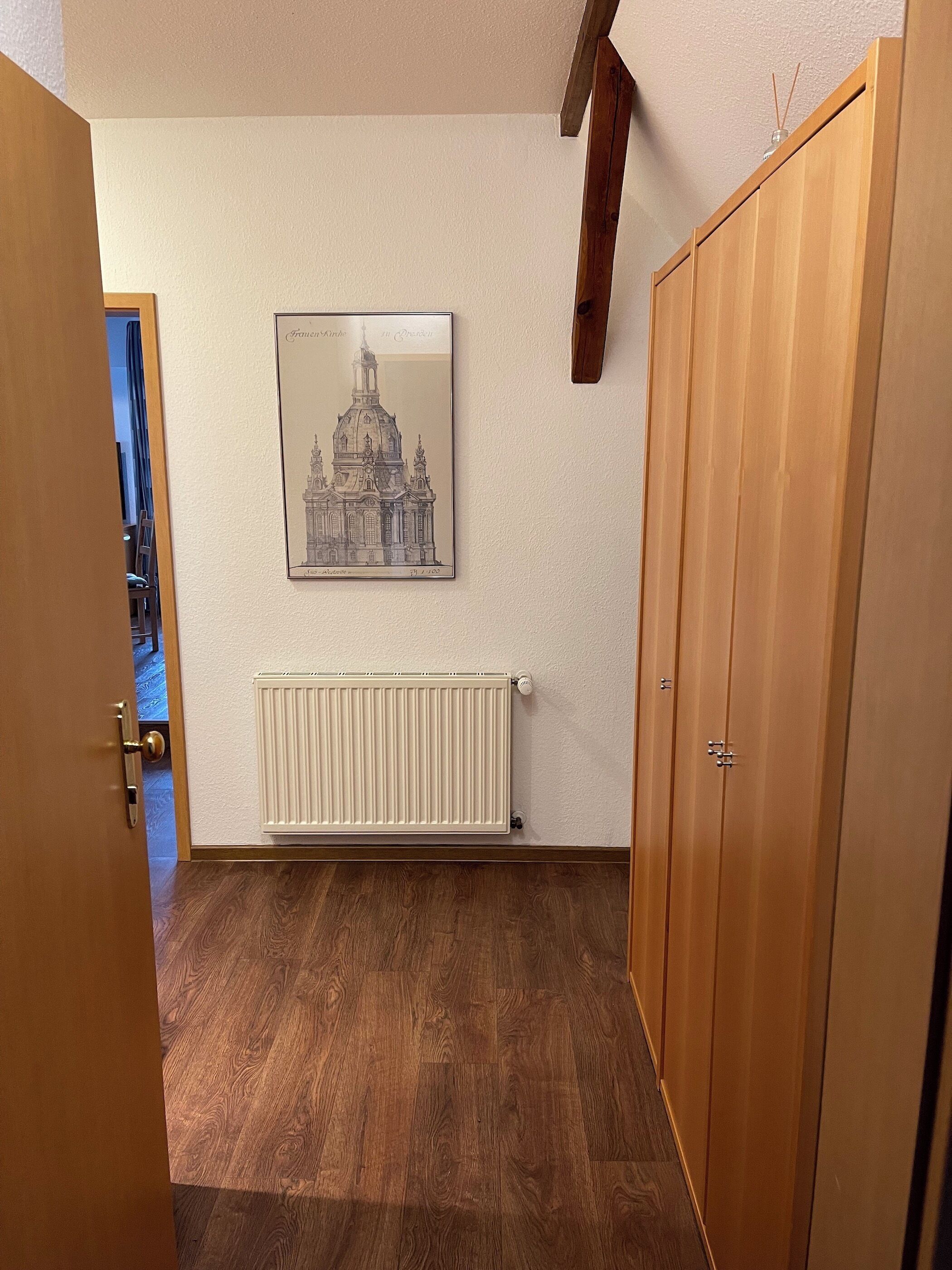 Una habitación con radiador, armario de madera y un dibujo arquitectónico enmarcado en la pared.