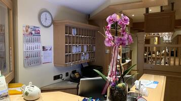 A reception area with a wooden desk, a clock, a calendar, and a shelf with glassware.