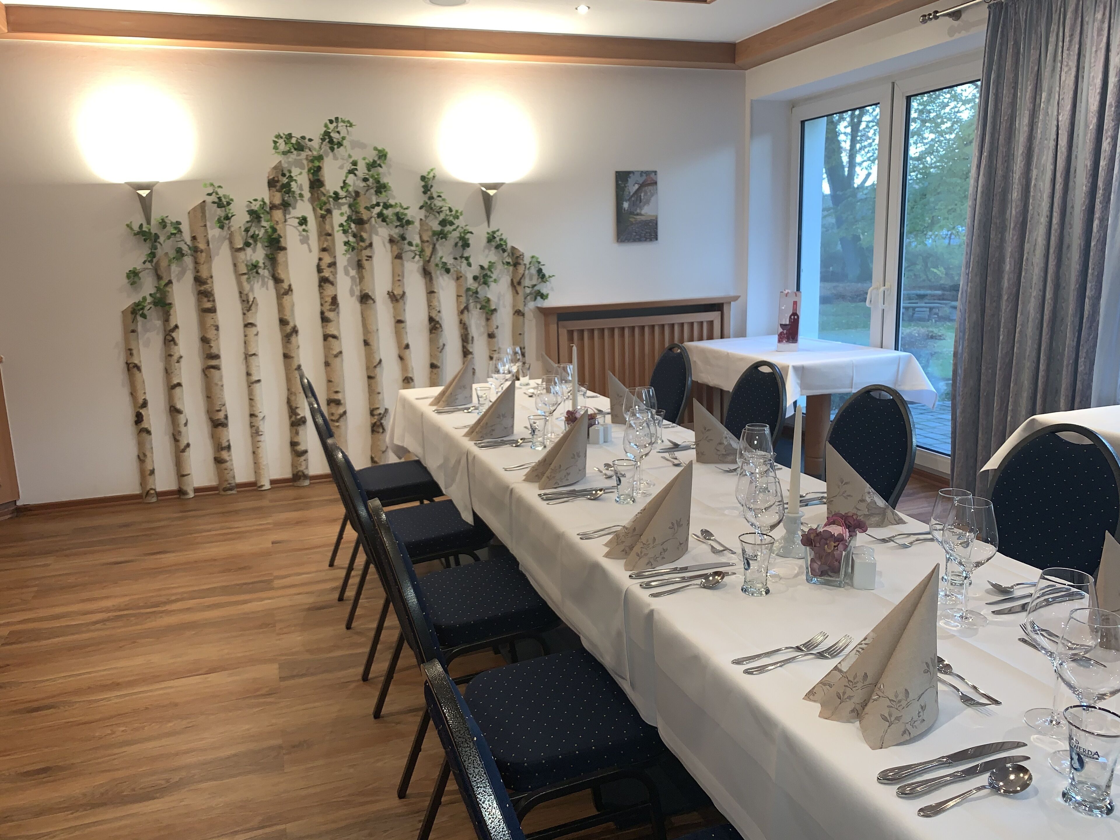 A dining area with a long table set for a meal, chairs, and a decorative wall with birch trees.