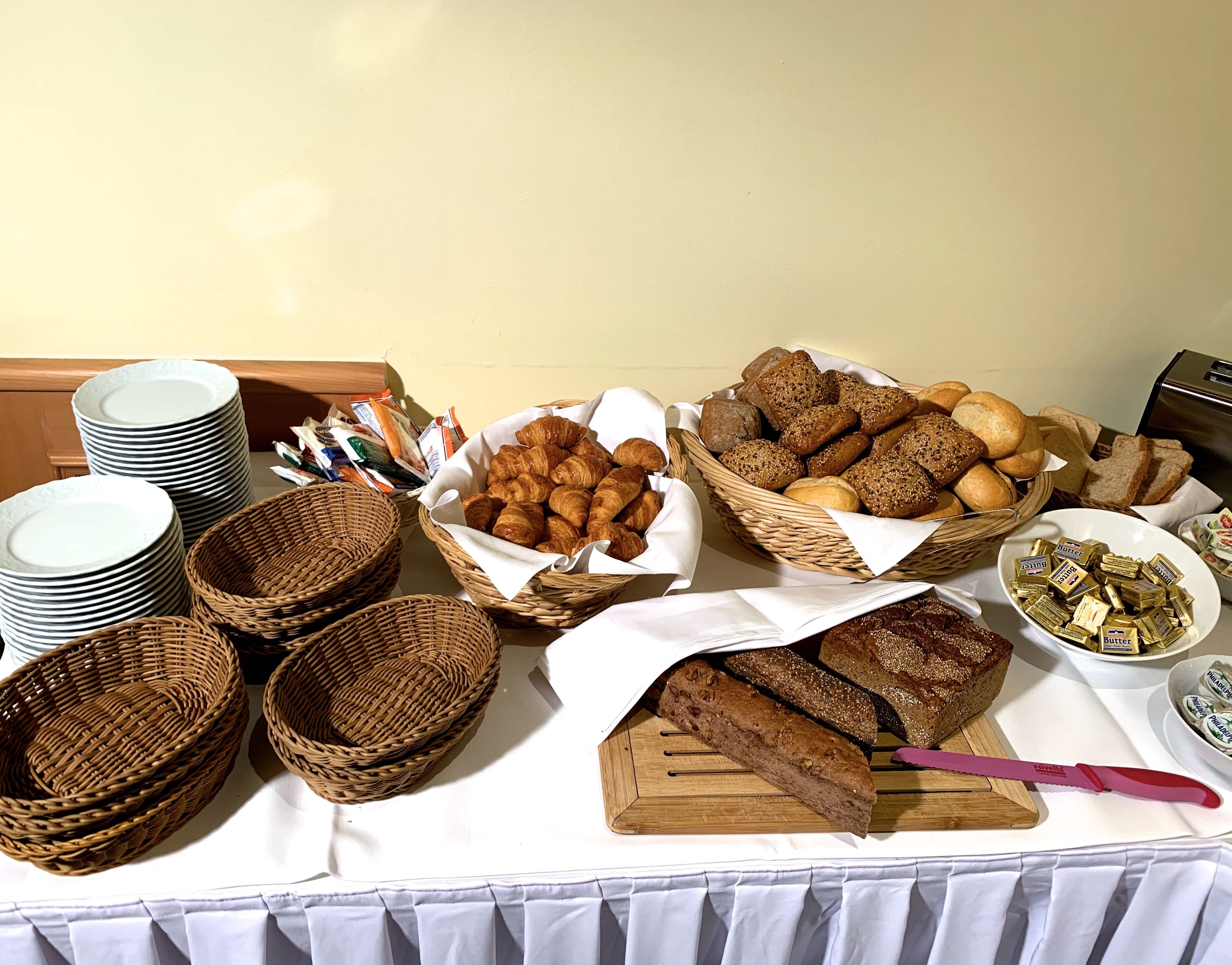 A buffet table with various breads, pastries, and butter.