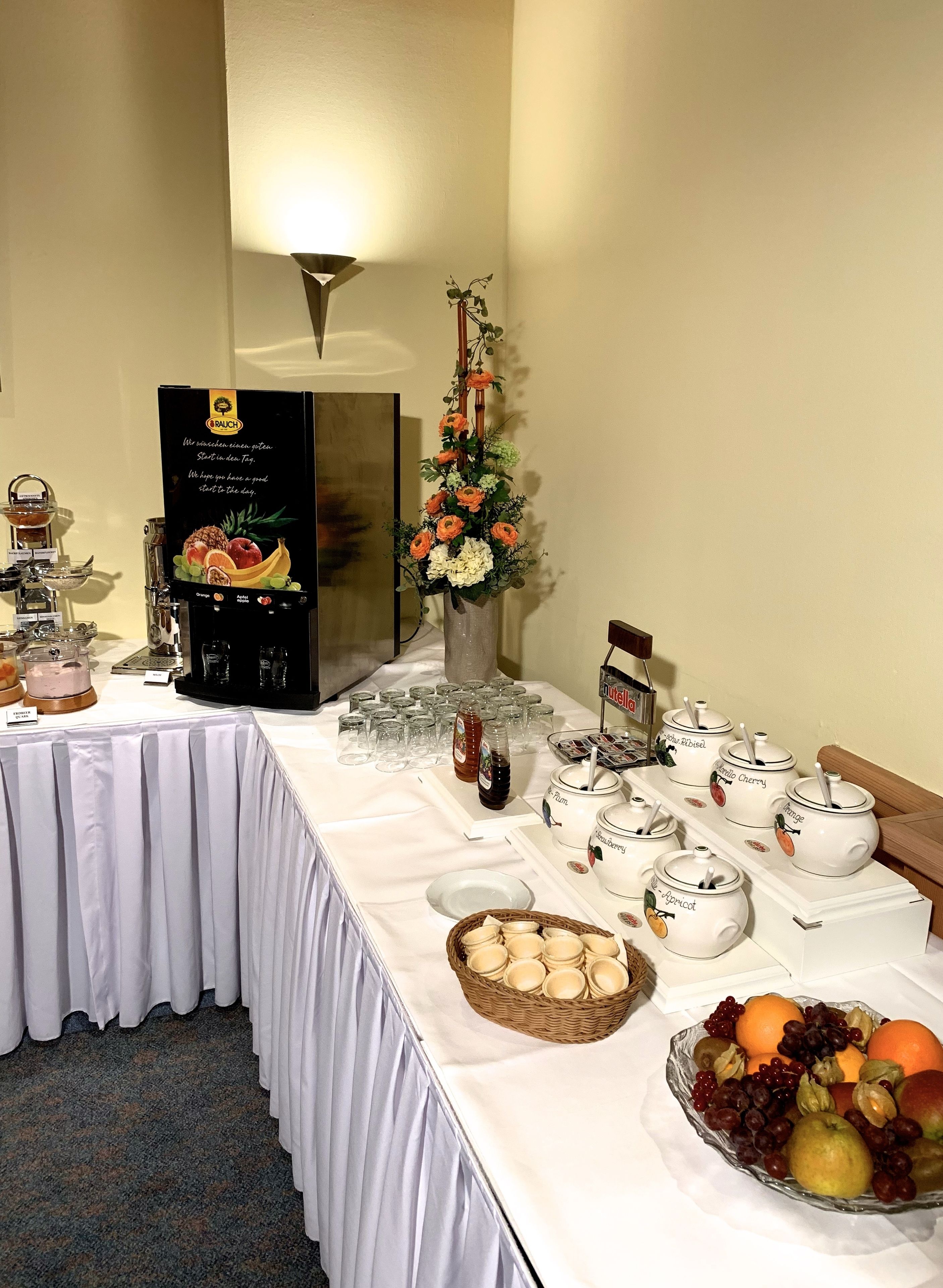 A buffet setup with various food items, including a fruit bowl, tea pots, and a beverage dispenser.