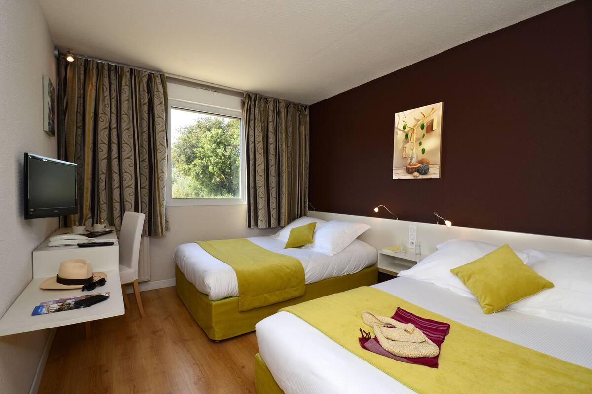 A hotel room with two beds, a desk with a TV, and a window with curtains.