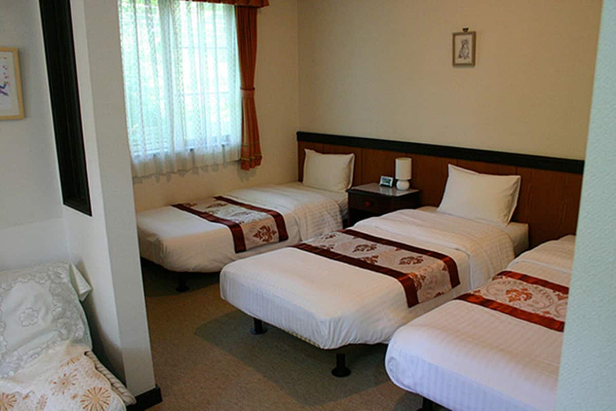 A hotel room with two single beds, a nightstand with a lamp, and a window with curtains.