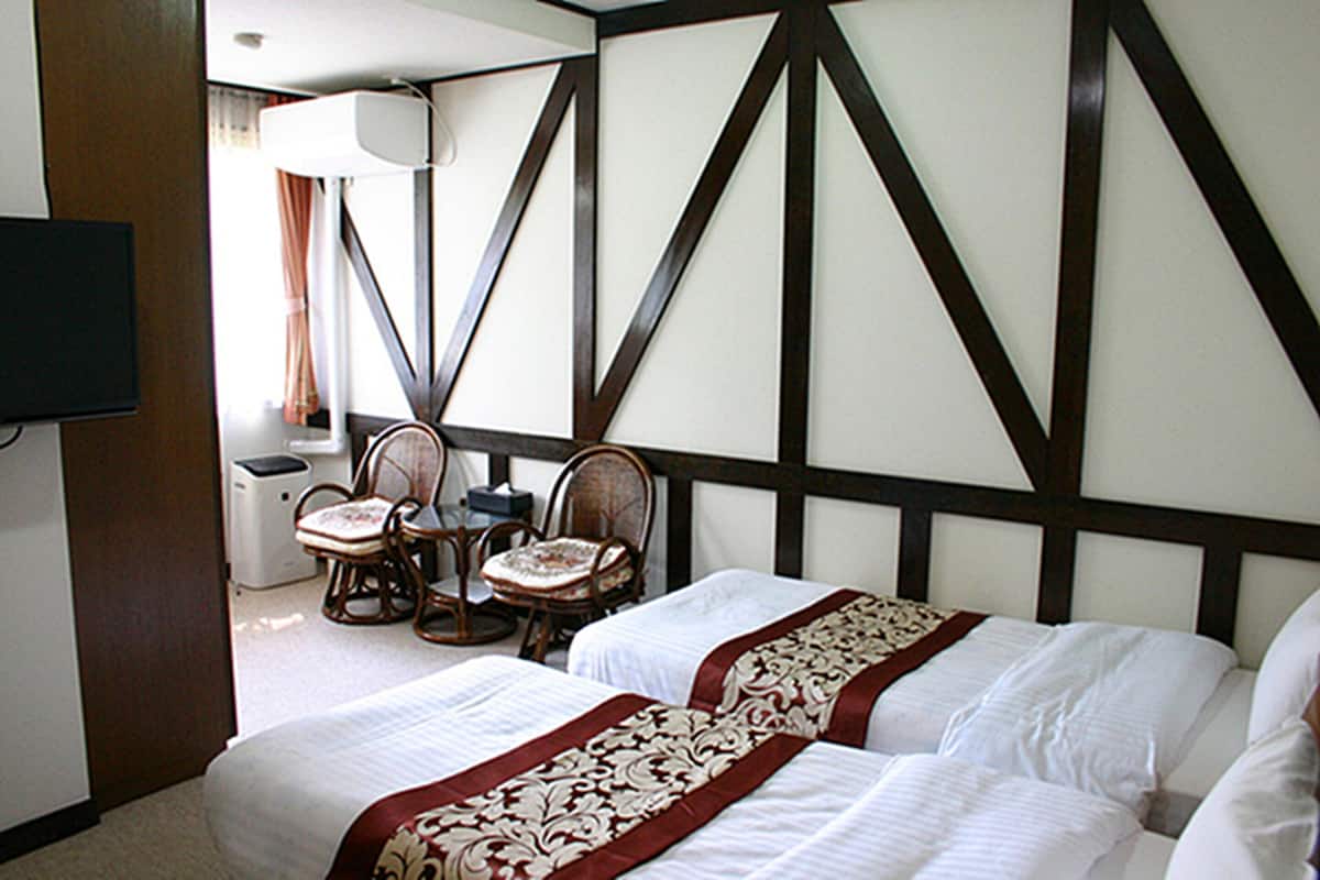 A hotel room with two beds, a television, a desk with a chair, and a window with curtains.
