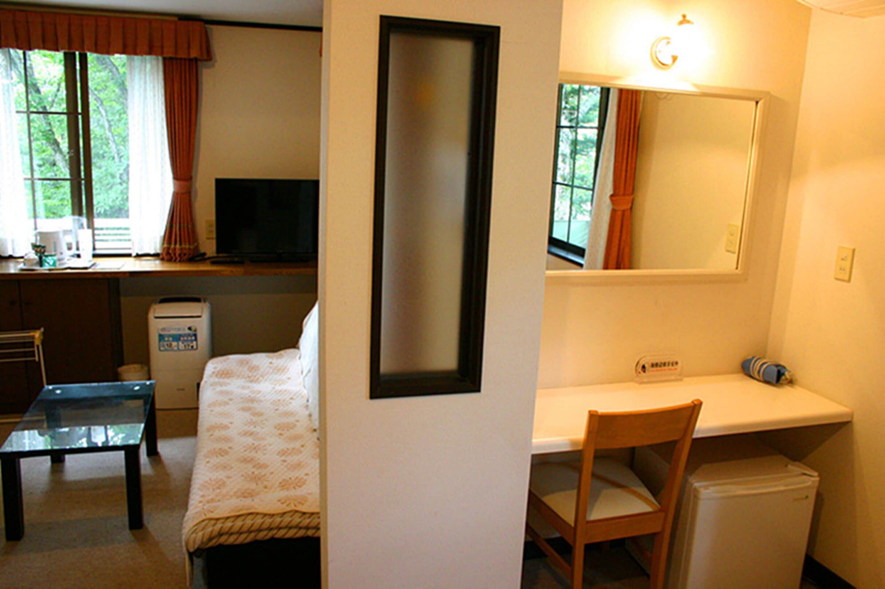 A compact room with a bed, a desk, a chair, a small table, a refrigerator, and a television.