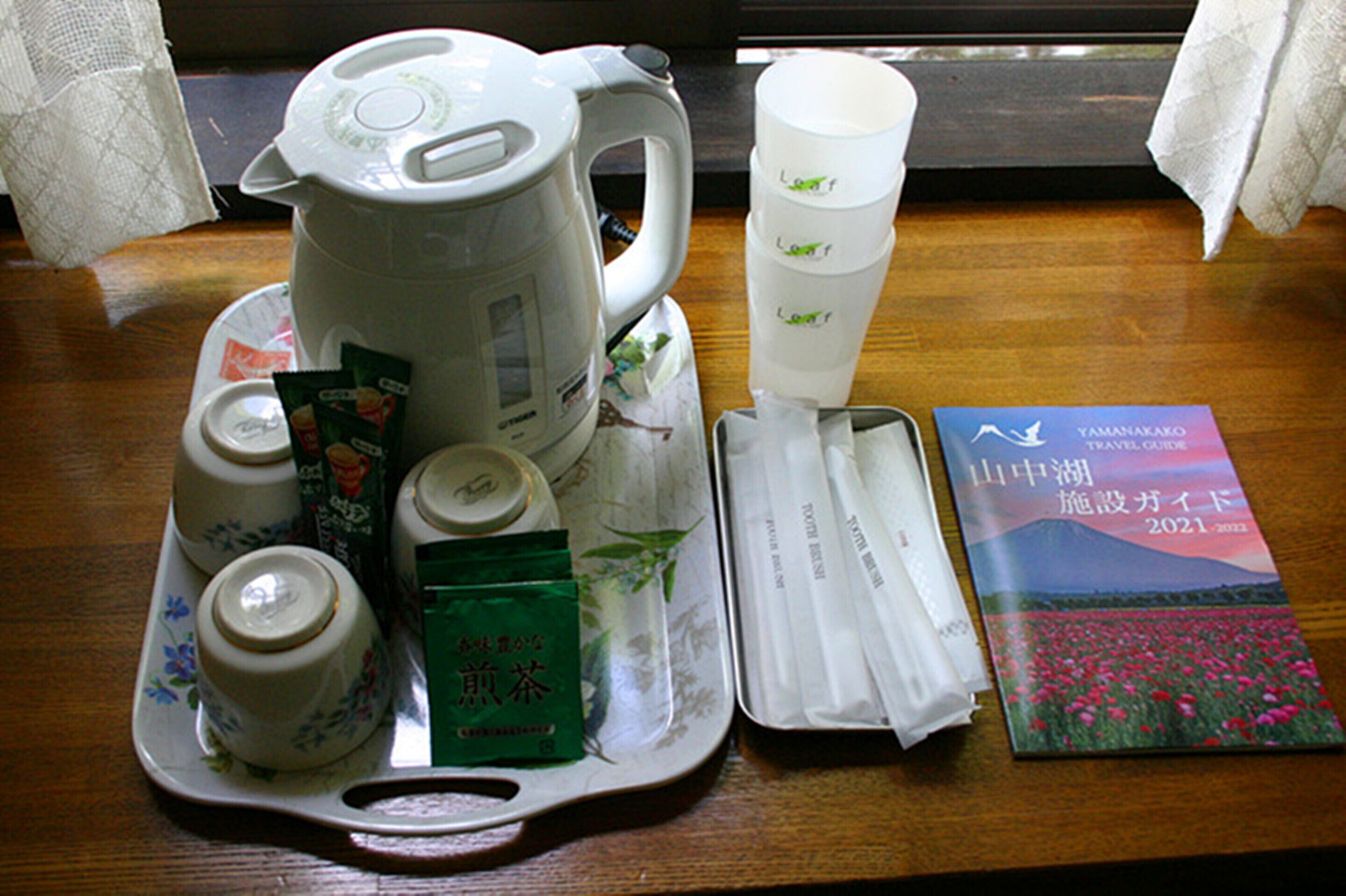 A tray with a tea kettle, cups, tea packets, and a travel guide on a wooden table.