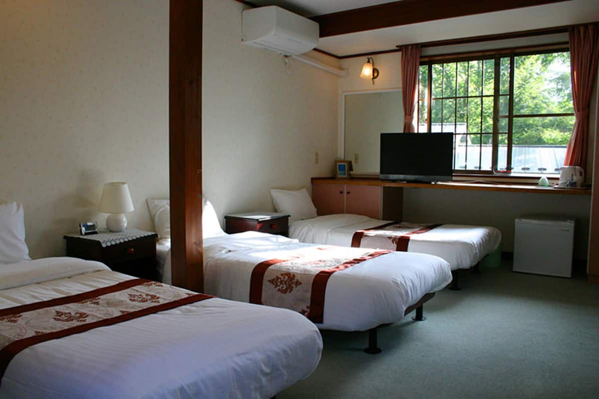 A hotel room with three single beds, a television, a small refrigerator, and a window with curtains.