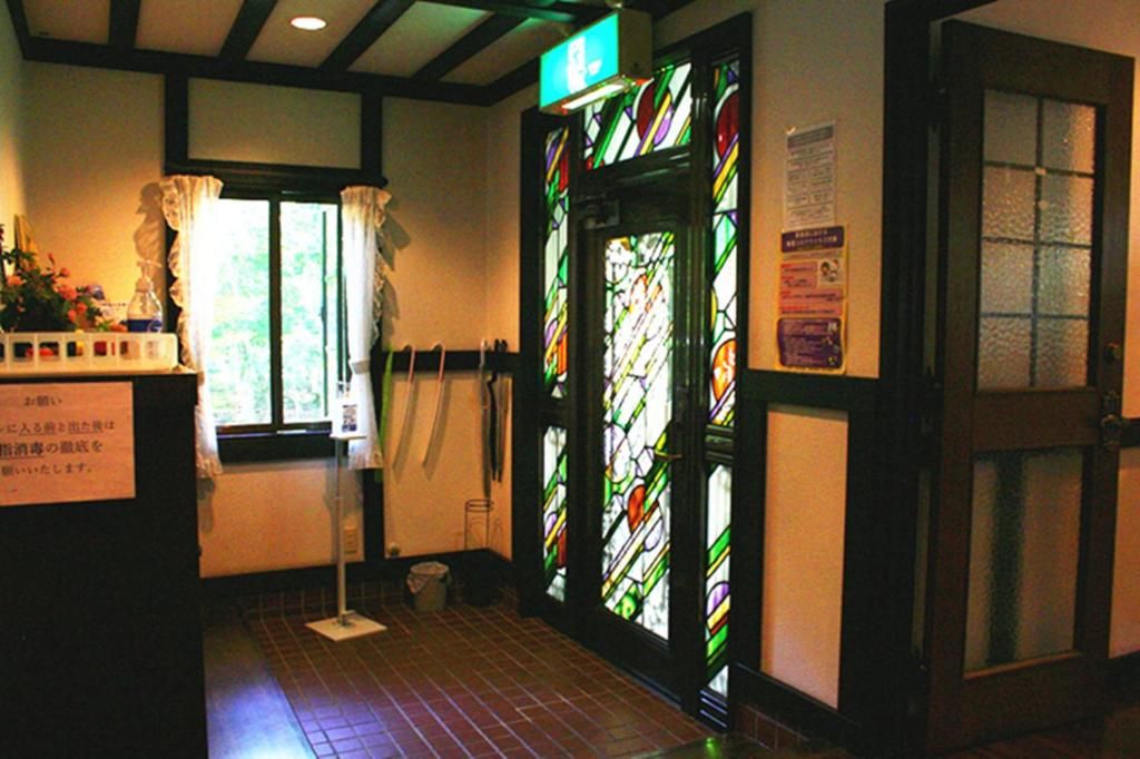 A hallway with a stained glass door, a window with curtains, and a sign on the wall.