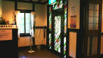 A hallway with a stained glass door, a window with curtains, and a sign on the wall.