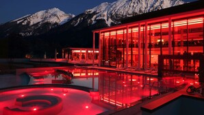 Un edificio moderno con fachada de vidrio y una zona de piscina, con montañas nevadas al fondo.