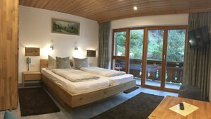 Un dormitorio con cama de madera, mesitas de noche, un televisor y un ventanal con vistas a zonas verdes.