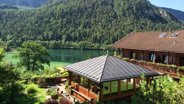 Una cabaña de madera con un porche acristalado que da a un lago y montañas.