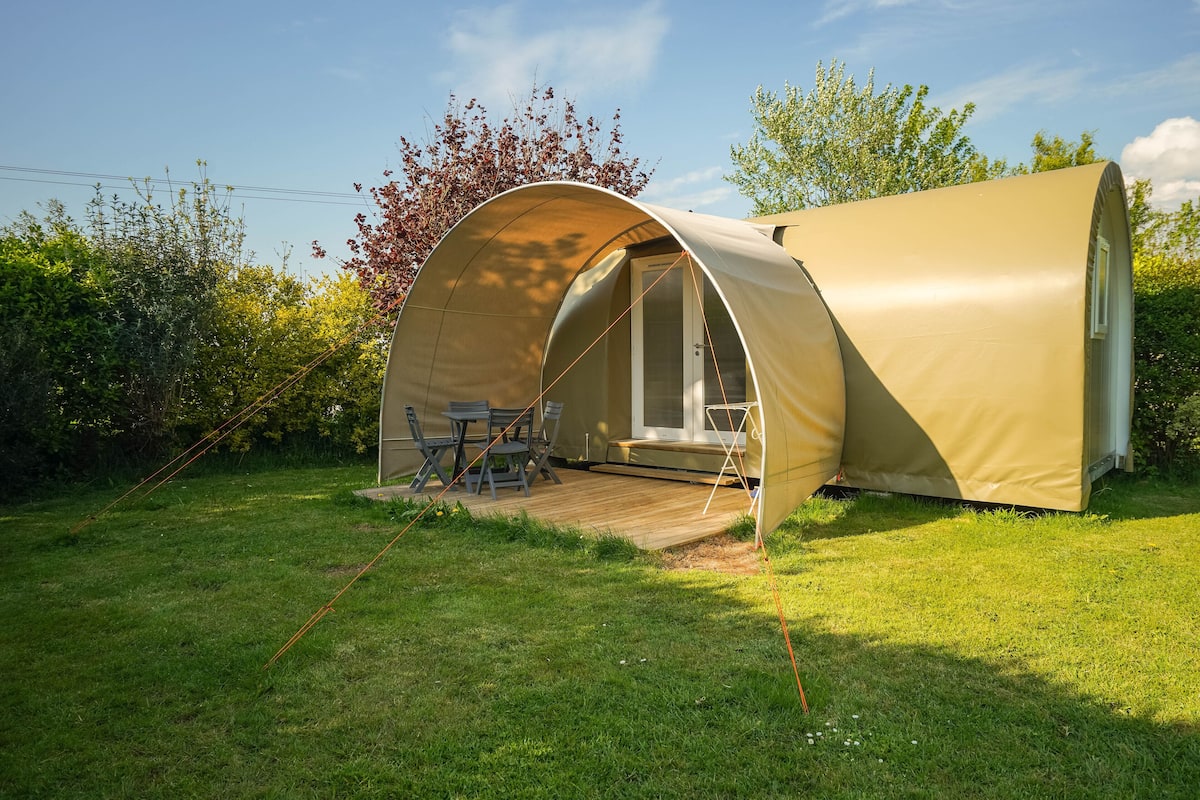 Une tente en forme de dôme dotée d’une terrasse en bois et d’un espace salon, le tout entouré de verdure.