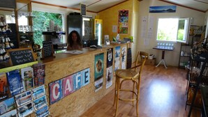 A cafe with a wooden counter, a woman behind the counter, and various posters on the wall.