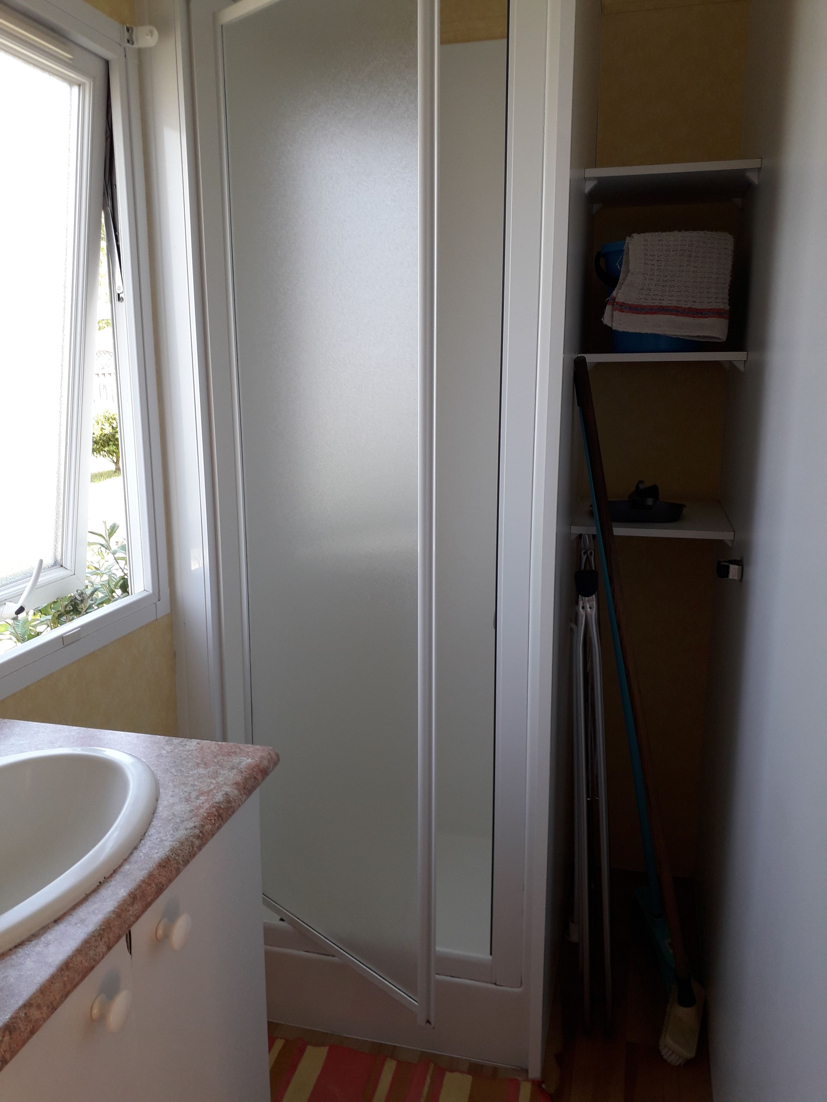 A bathroom with a white sink, a shower door, and a shelf with a towel.