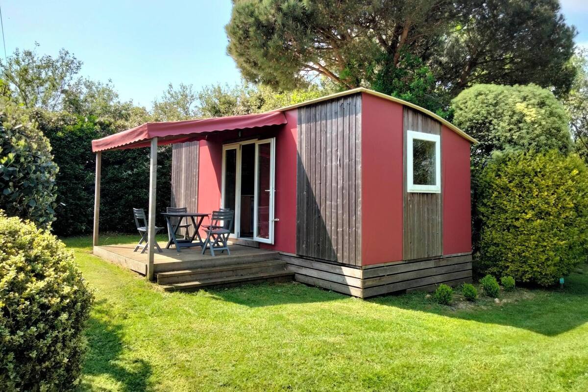 Une petite structure en bois rouge, dotée d’un patio couvert, d’une porte-fenêtre coulissante et d’une petite fenêtre.