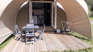 A dome-shaped tent with a kitchen area visible through the entrance, a dining table with chairs, and a small outdoor seating area.